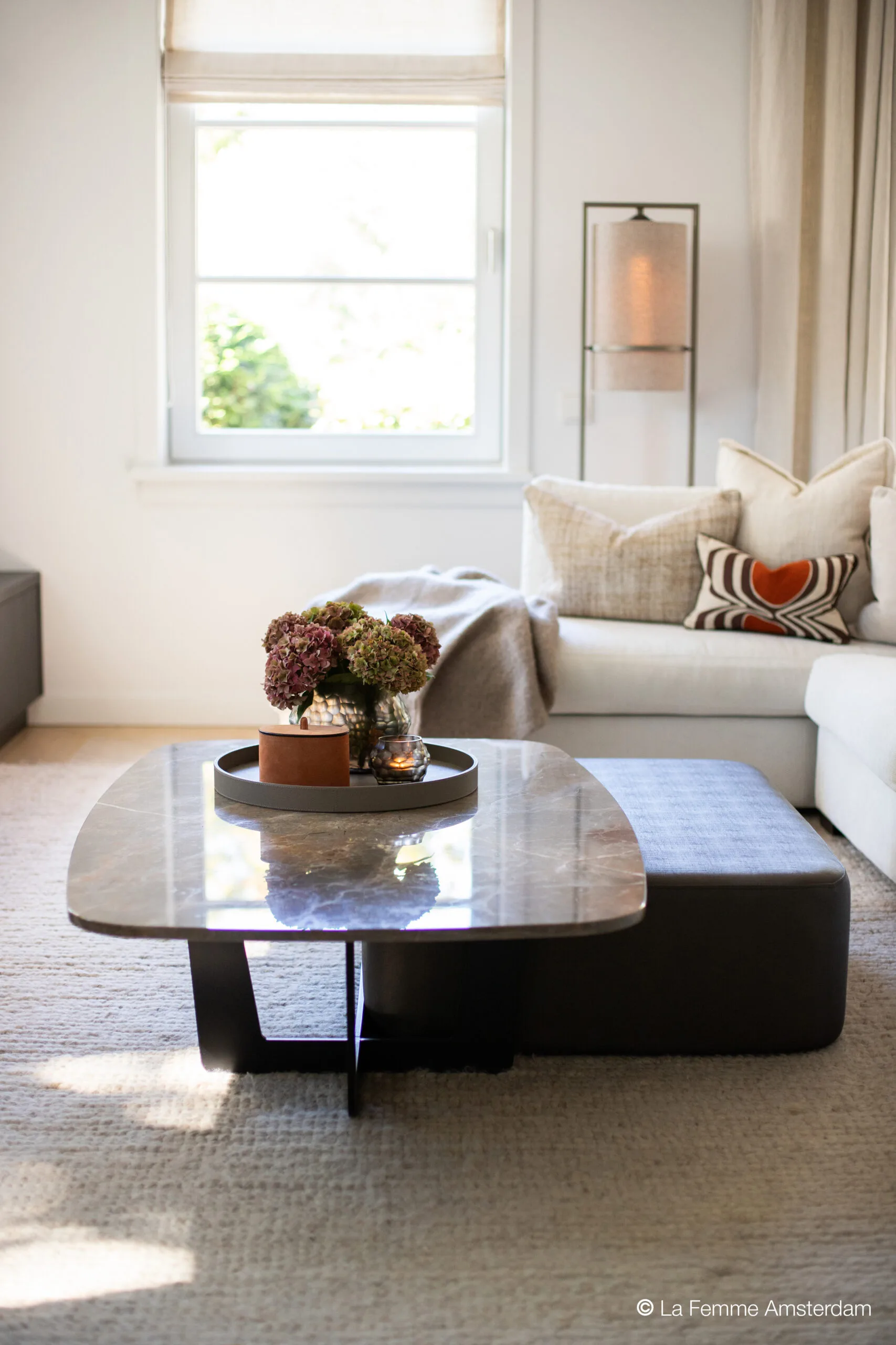 Close-up of the Venice coffee table with a polished stone top and sculptural black base, styled with a round tray, vases, and flowers in a serene living room setting.
