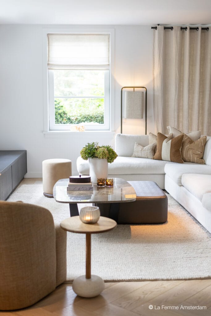 Modern living room with the Lucena coffee table featuring a rounded rectangular stone top and dark sculptural base, styled with books, candles, and floral decor.