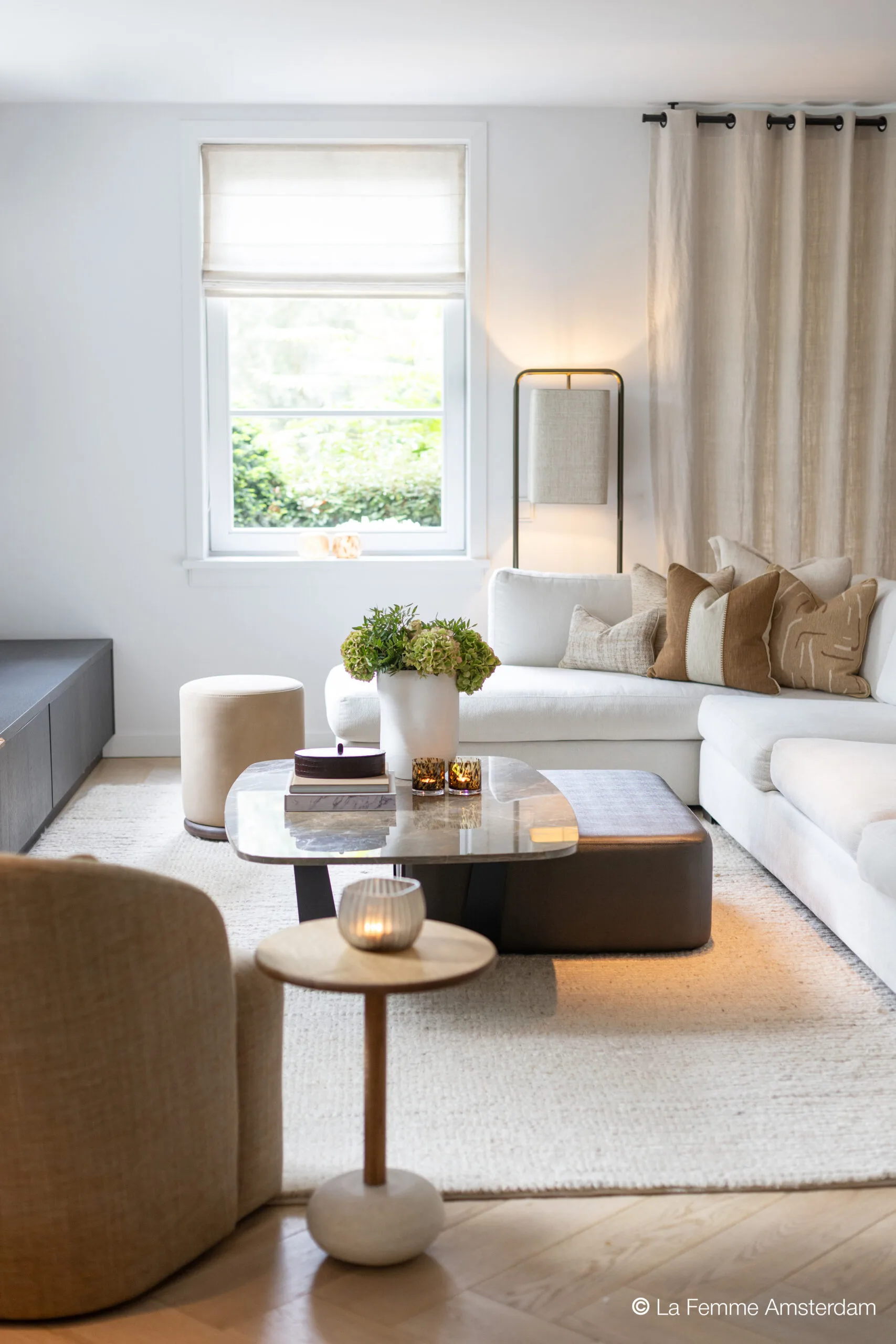 Modern living room with the Lucena coffee table featuring a rounded rectangular stone top and dark sculptural base, styled with books, candles, and floral decor.