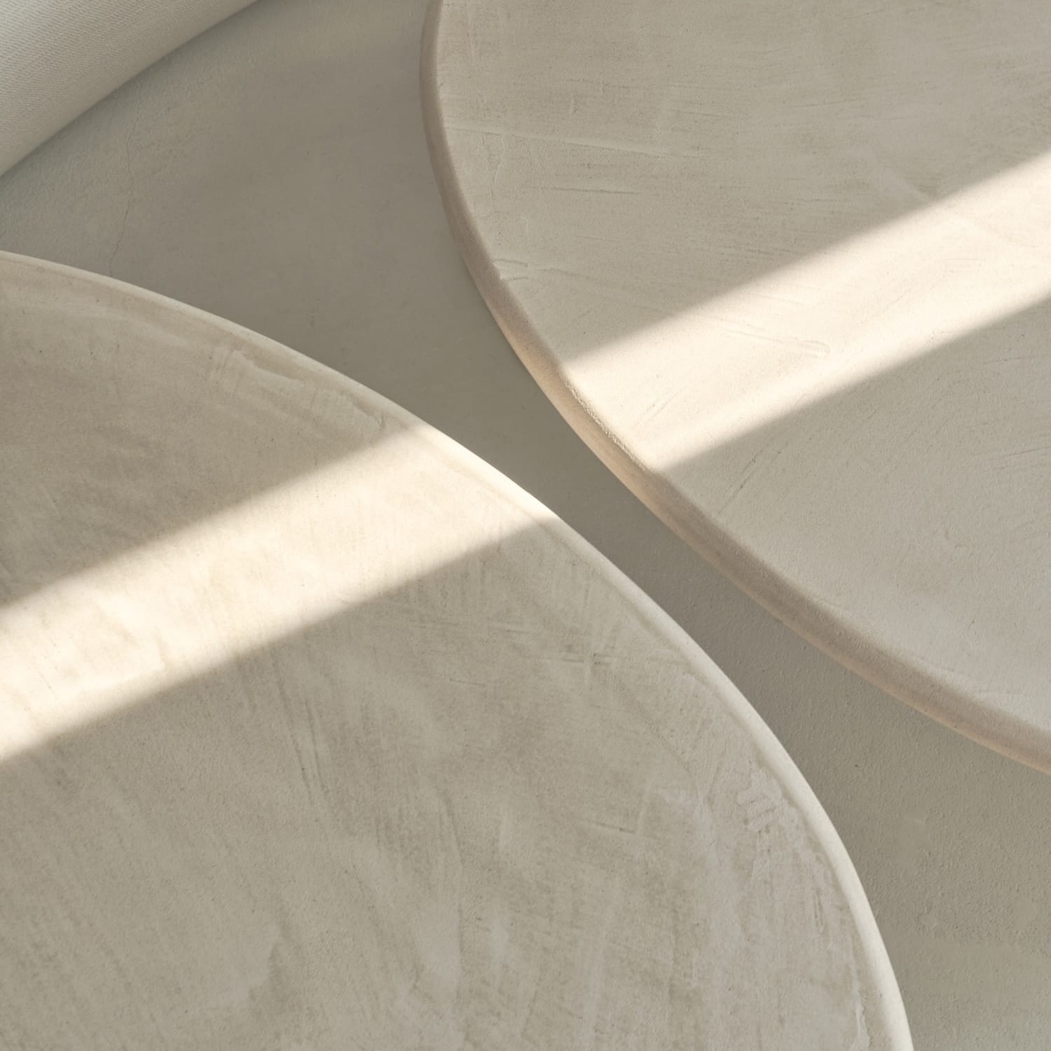 Close-up of two round, stucco tabletops with a textured matte finish, highlighted by soft natural light.