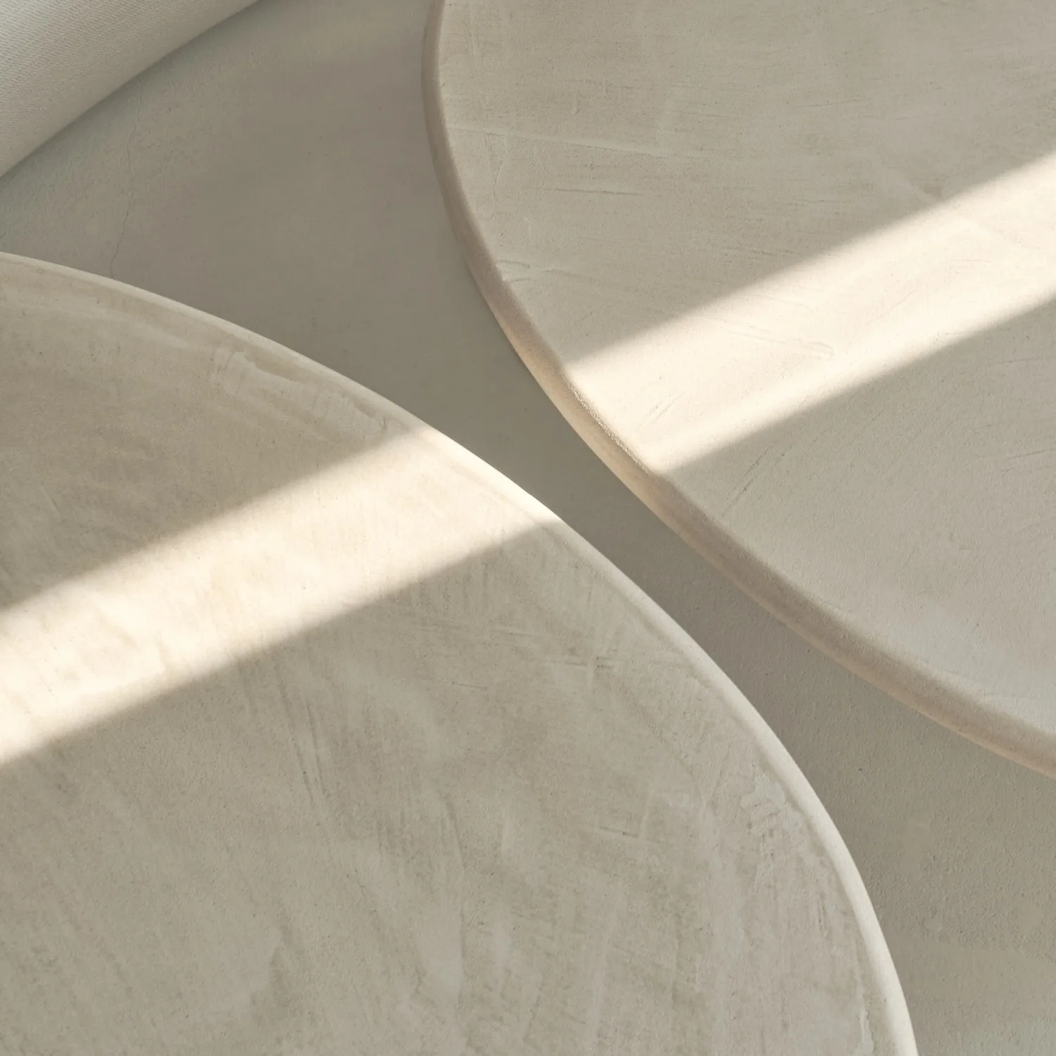 Close-up of two round, stucco tabletops with a textured matte finish, highlighted by soft natural light.