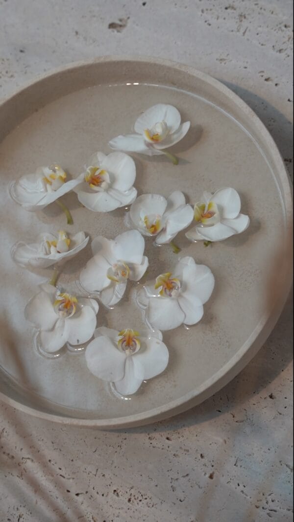 Close-up of white orchid flowers floating in a beige Bola bowl filled with water.