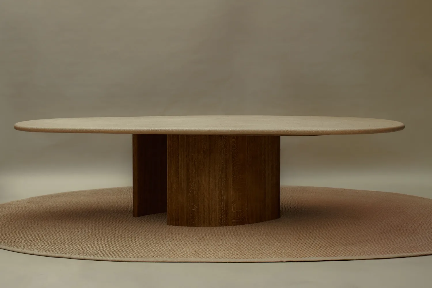 Straight-on view of the Caprice dining table, placed on a round beige rug under soft studio lighting.