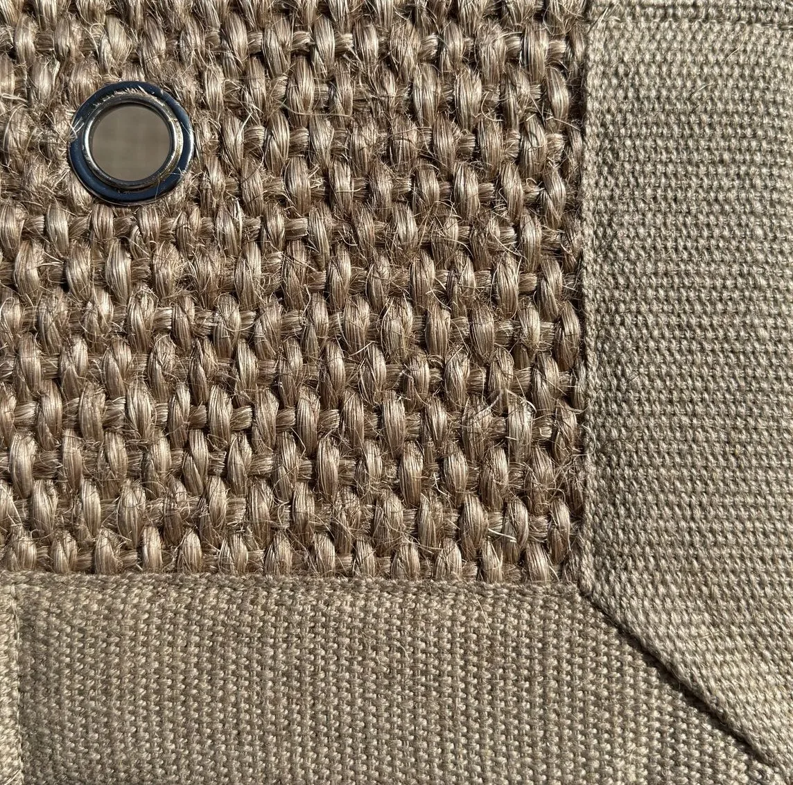Close-up of Sisal 04 in color 21, showing a tightly woven natural fiber texture with a fabric border and a metal eyelet.