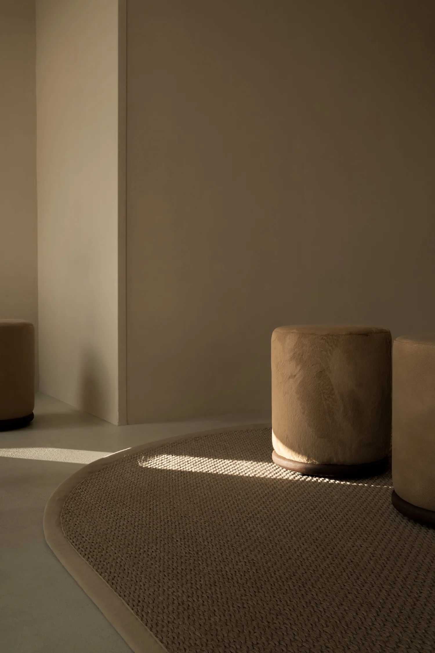 Three Ackley poufs in a warm-toned minimalist room, placed on a textured rug.