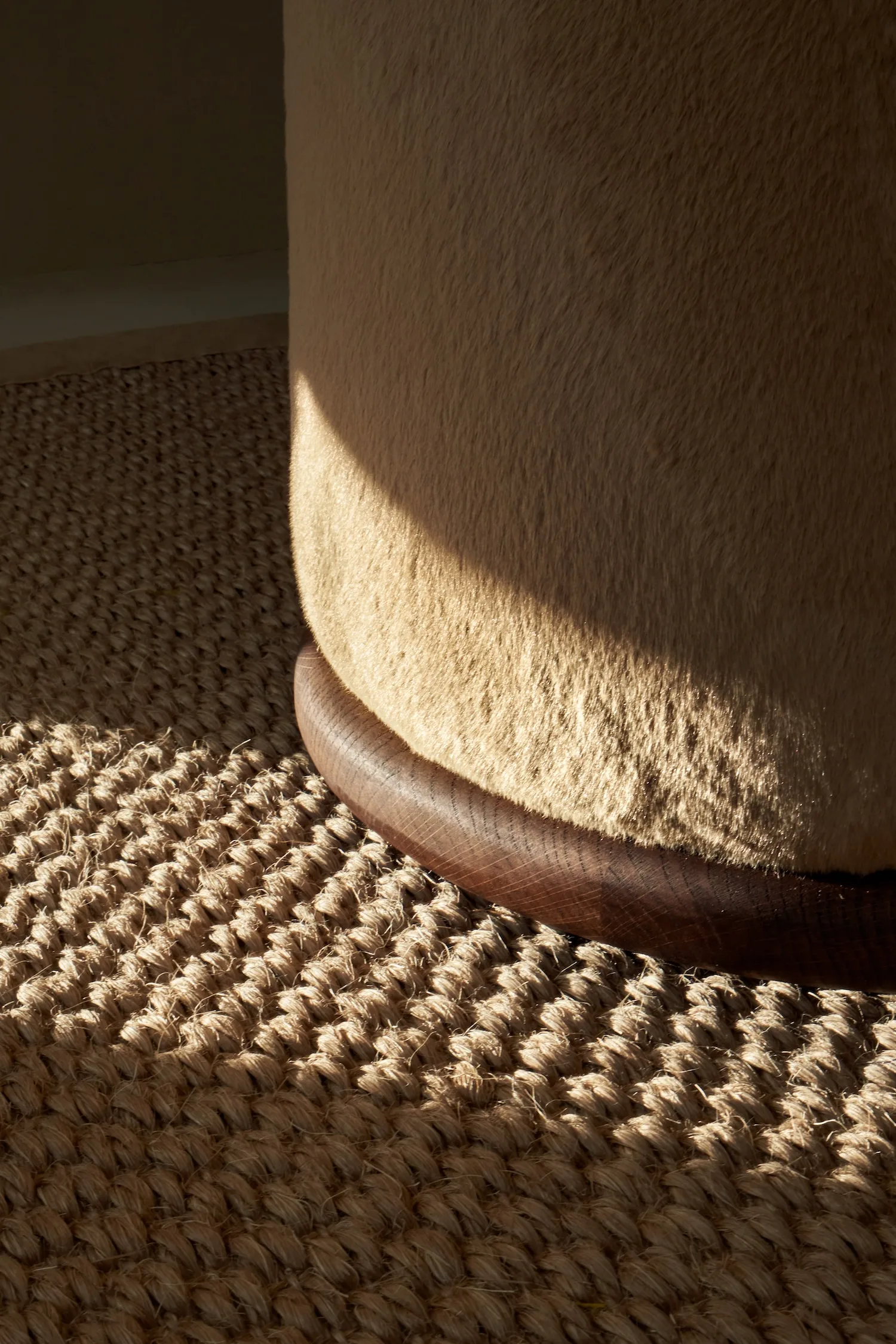 Detailed close-up of an Ackley pouf’s soft fabric and dark wooden base.