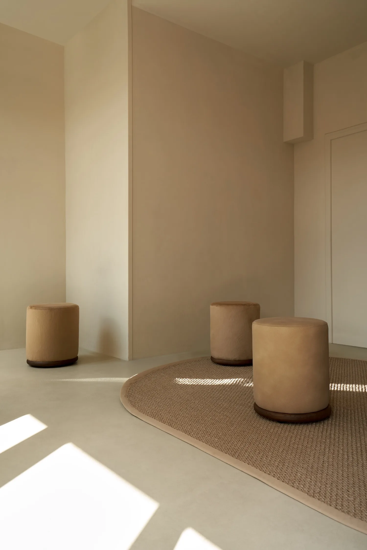 Bright, neutral-toned interior with three Ackley poufs on a curved jute rug.