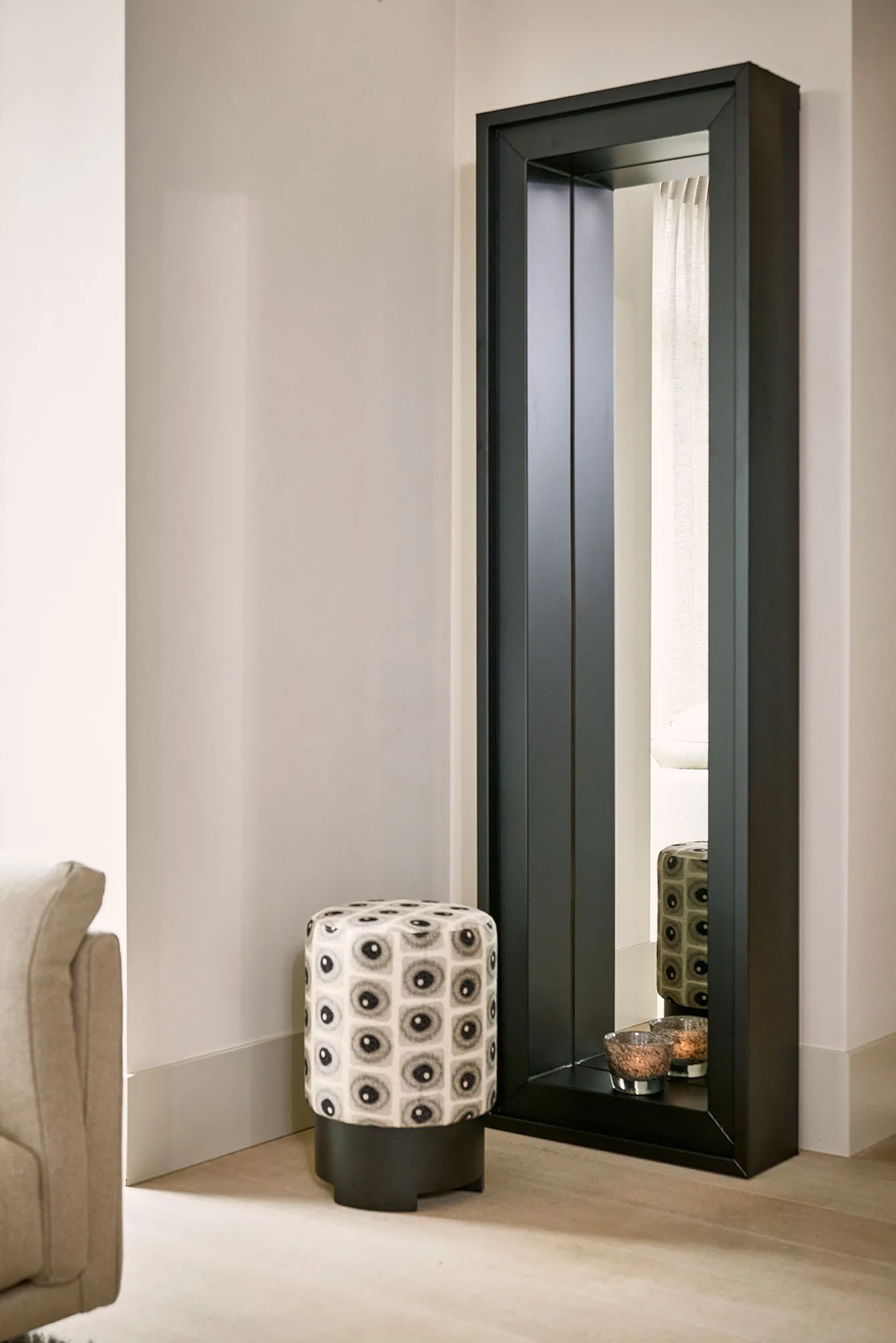 Black-framed Esquina mirror paired with a small patterned stool and soft interior lighting.