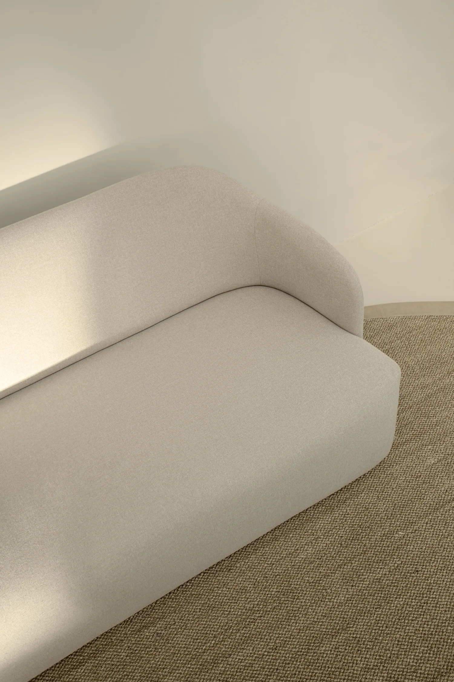 Top-down view of the August sofa in a light beige fabric, placed on a textured woven rug.