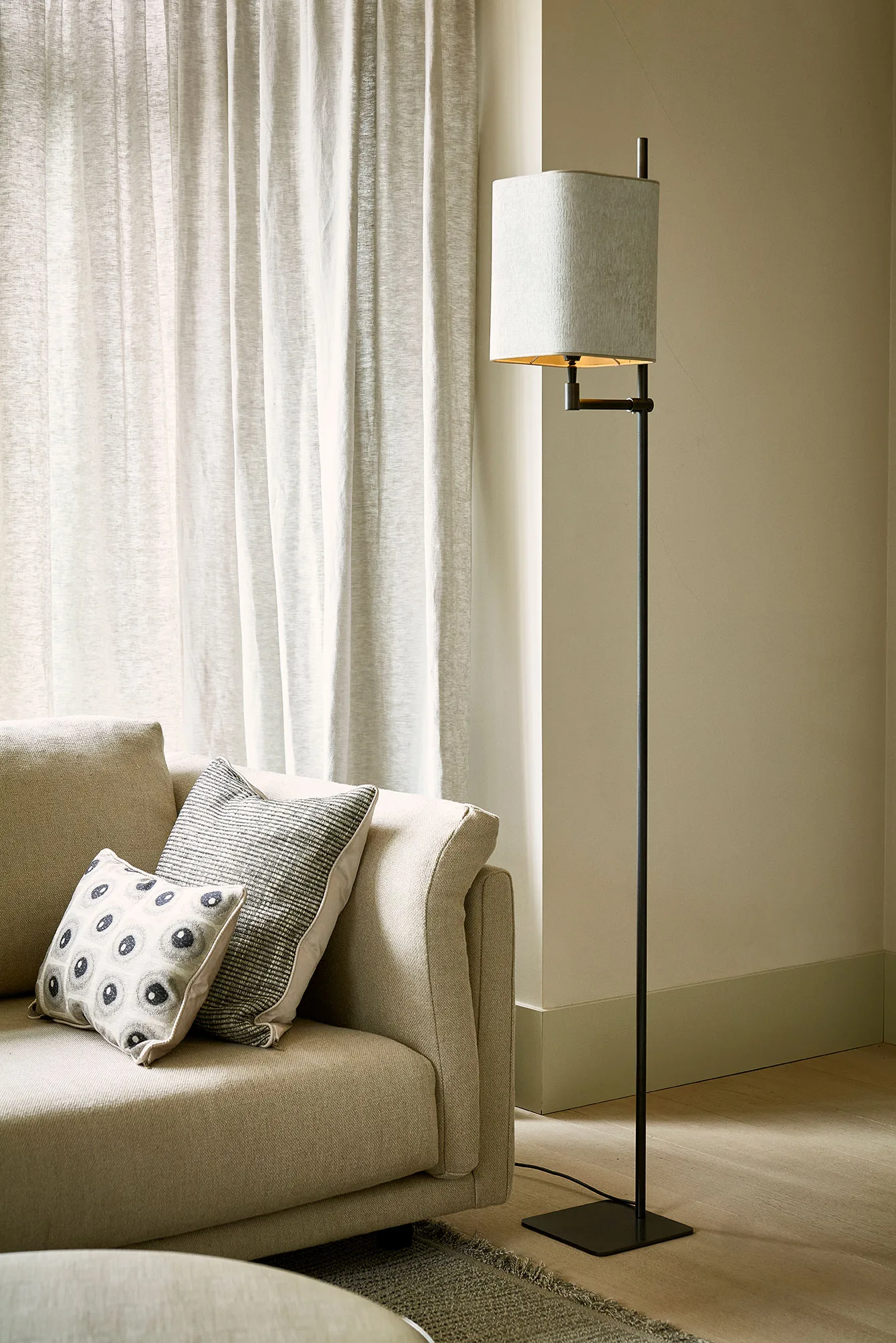 Ava floor lamp with a rectangular cream shade beside a beige sofa and sheer curtains.