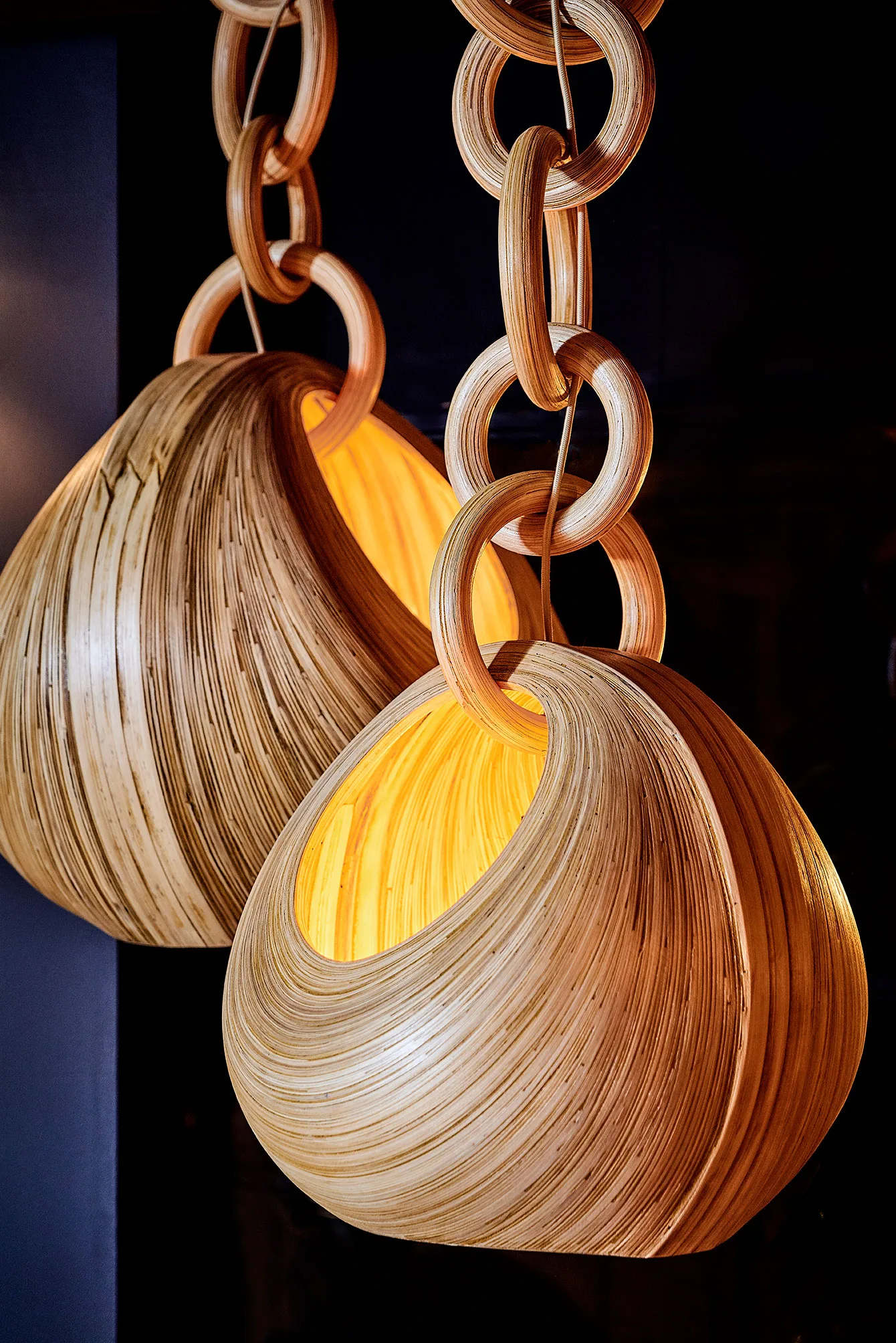 Pair of sculptural bamboo pendant lights with glowing interiors, suspended by thick linked bamboo chains.