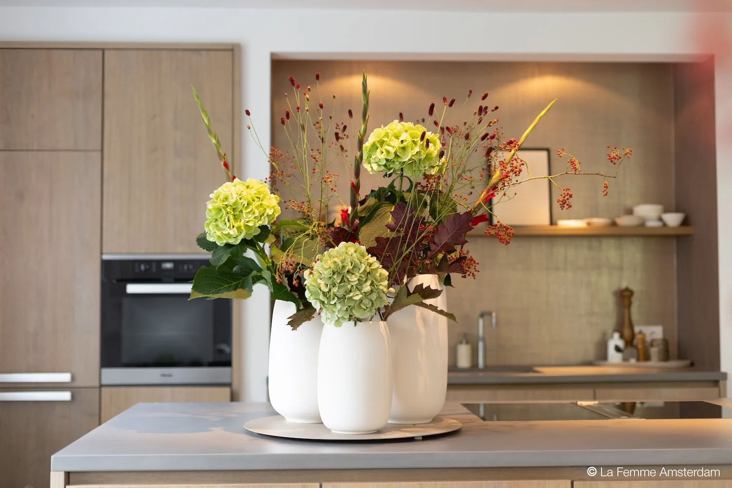 Three white Bola vases filled with colorful flowers displayed on a modern kitchen island.