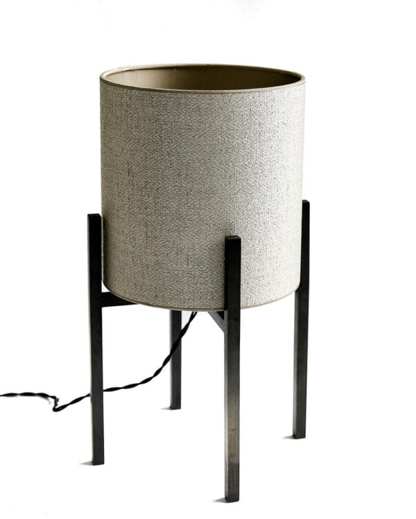 Cylindrical lamp with textured shade and four-legged metal base, placed on a stone tabletop.