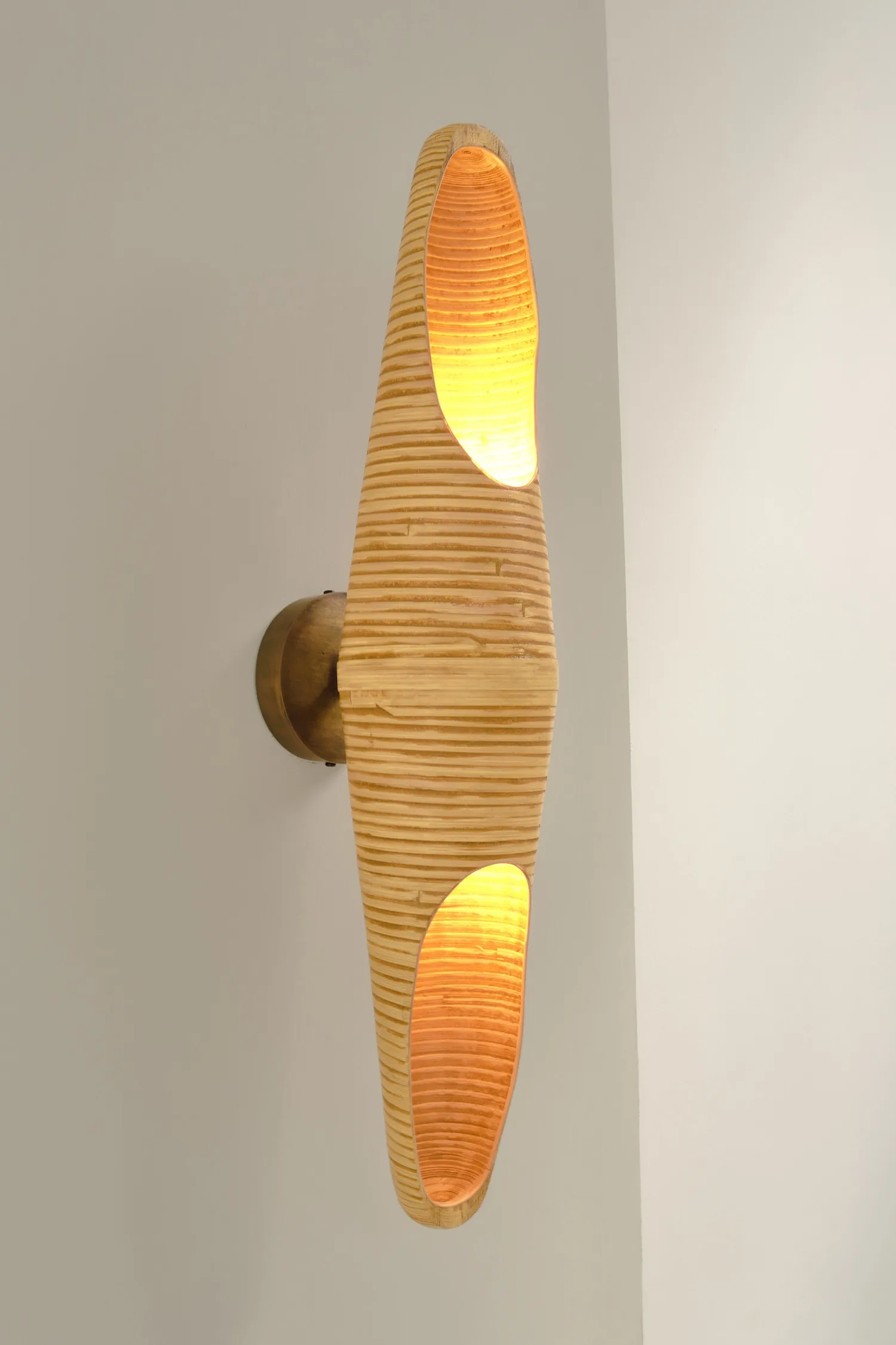 Cocoon wall light in natural rattan, with a sculptural hourglass shape and warm inner glow.