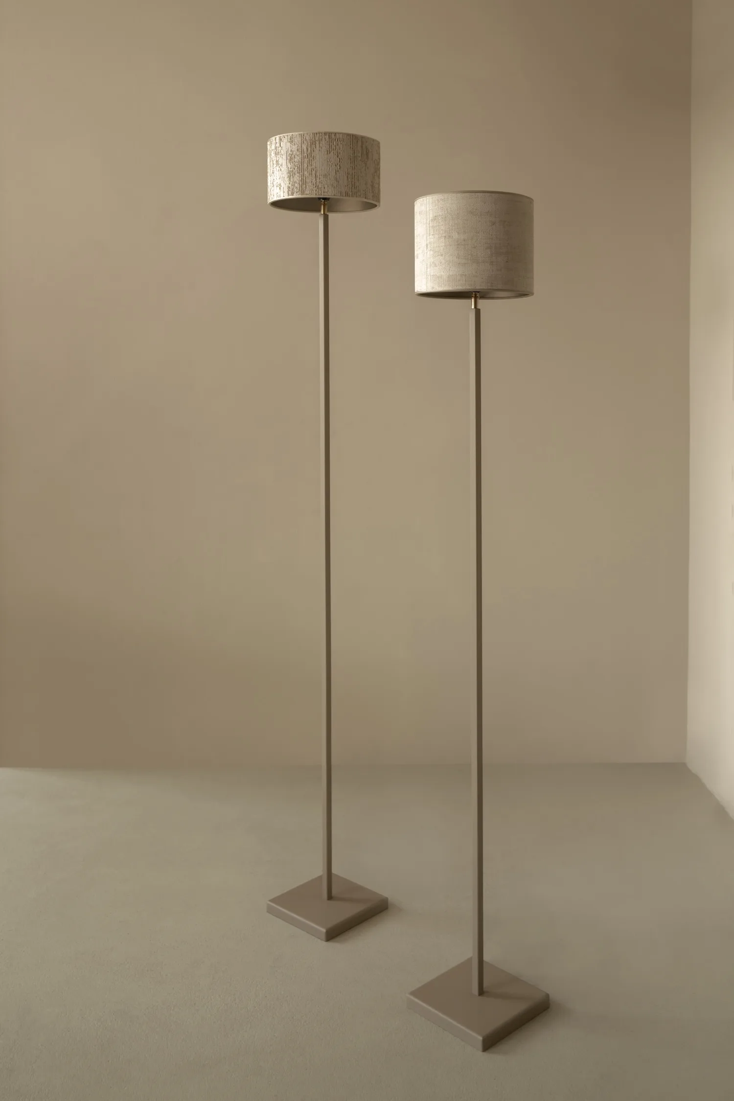 Two Duld floor lamps with slim beige bases and round fabric lampshades in a neutral setting.