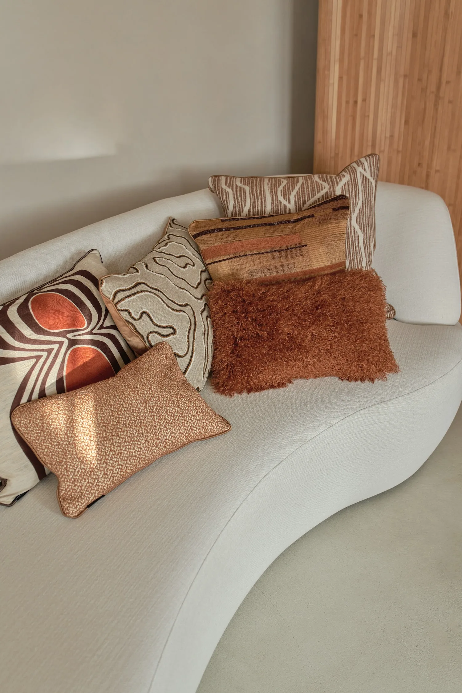 Assorted earth-toned decorative cushions with rich textures and patterns on a cream curved sofa.