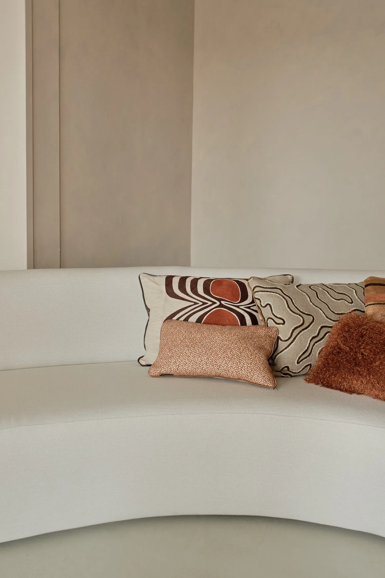 Front view of patterned and textured cushions in warm neutral shades on a light curved sofa.