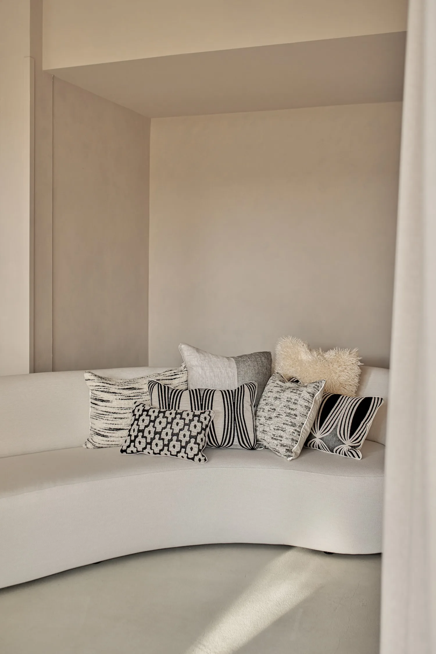 Collection of black and white patterned cushions with varied textures on a light curved sofa.