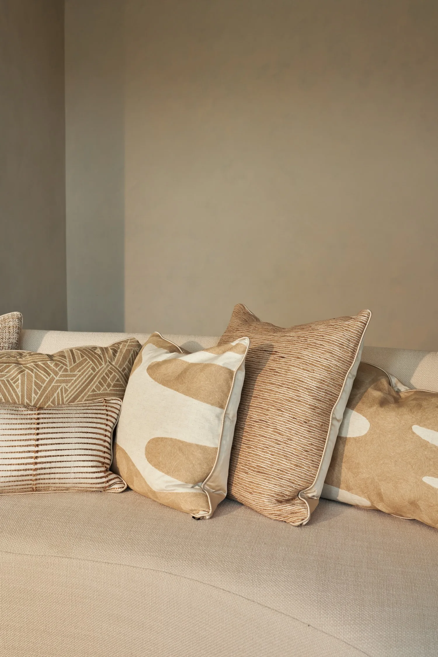 Close-up view of five decorative cushions with various textures and abstract patterns in natural hues.