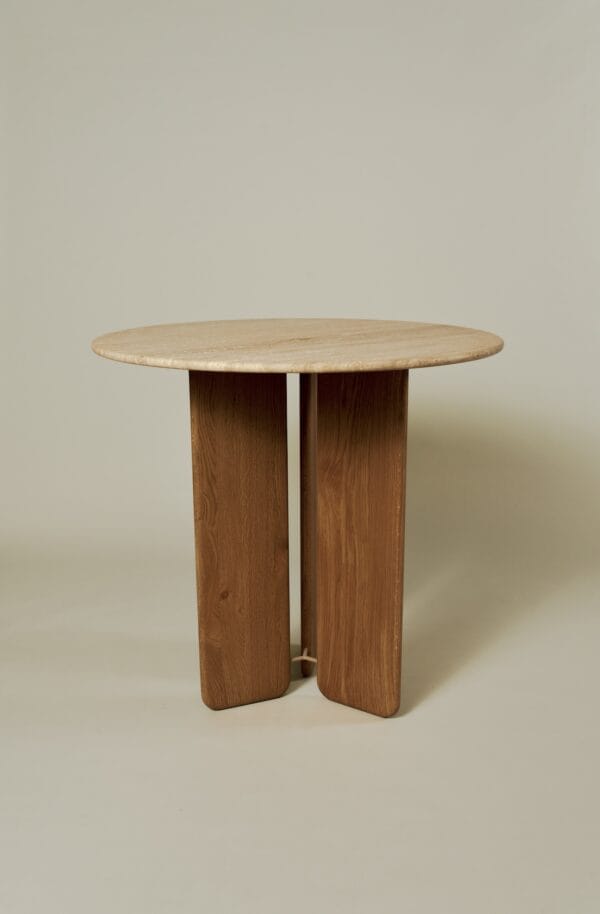 Emilia dining table with round travertine top and sturdy vertical wooden legs in a neutral setting.