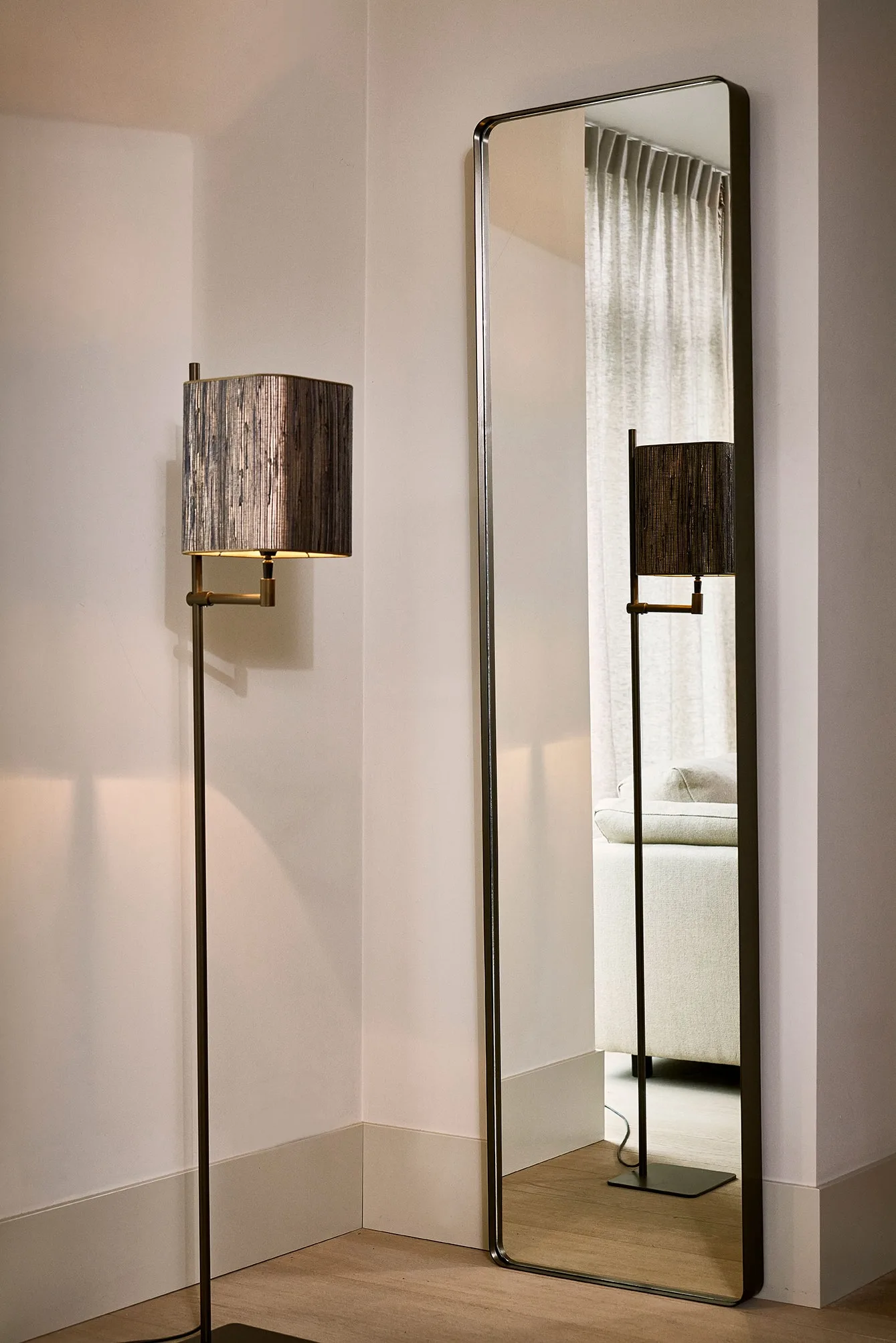 Tall rectangular Esquina mirror with rounded corners next to a modern floor lamp.