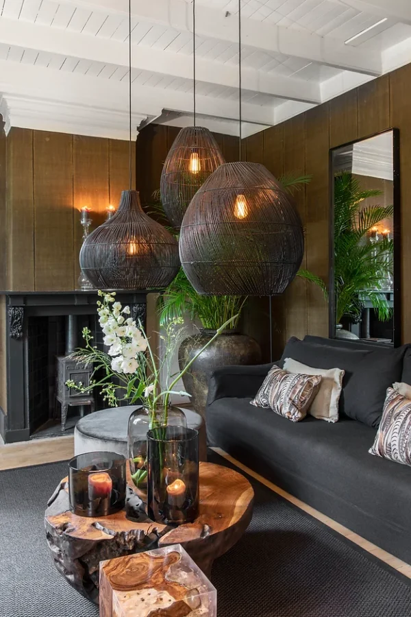 Three large, woven pendant lights from the Figura set hanging above a dark-toned lounge with natural decor.