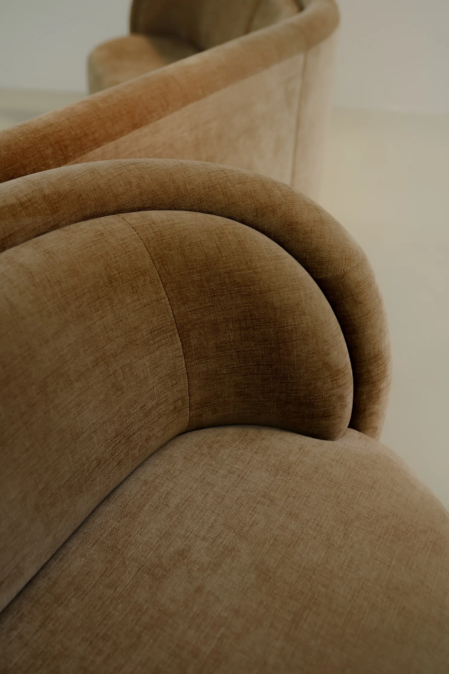 Detail view of the fabric and stitching on the armrest of a camel velvet Georgie modular sofa with curved forms and soft texture.