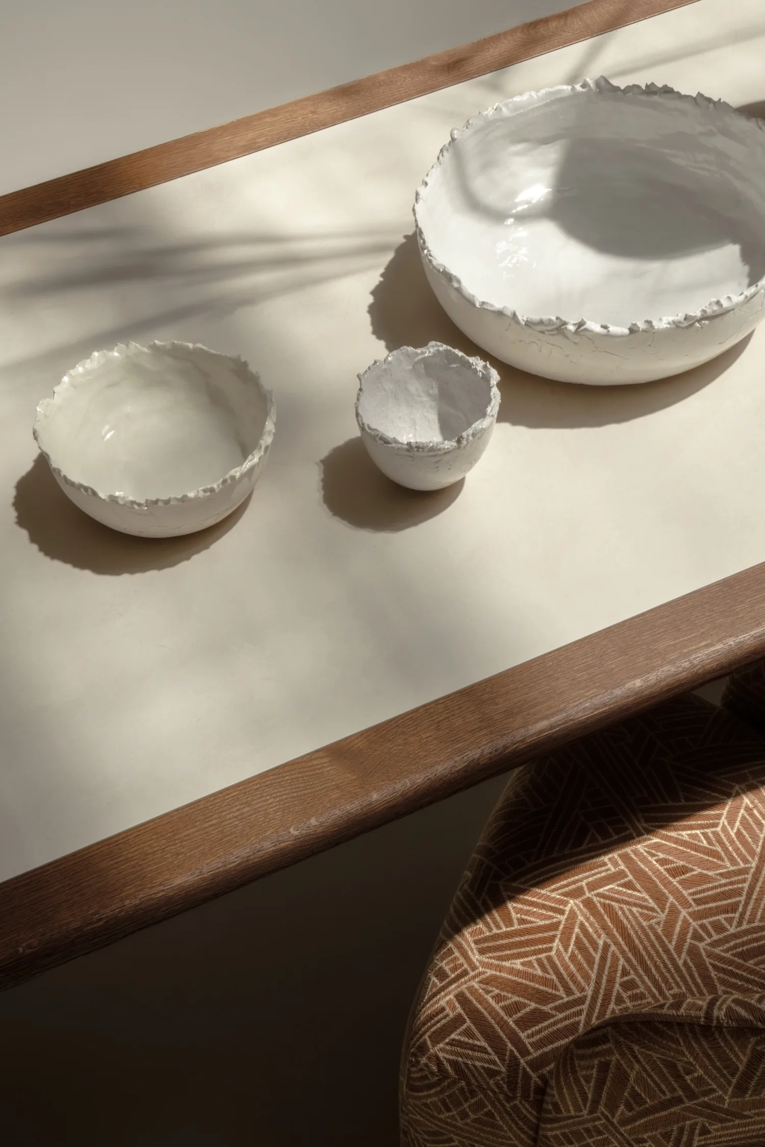 Top view of textured ceramic bowls on the Hudson table with soft shadows and patterned chair partially visible.