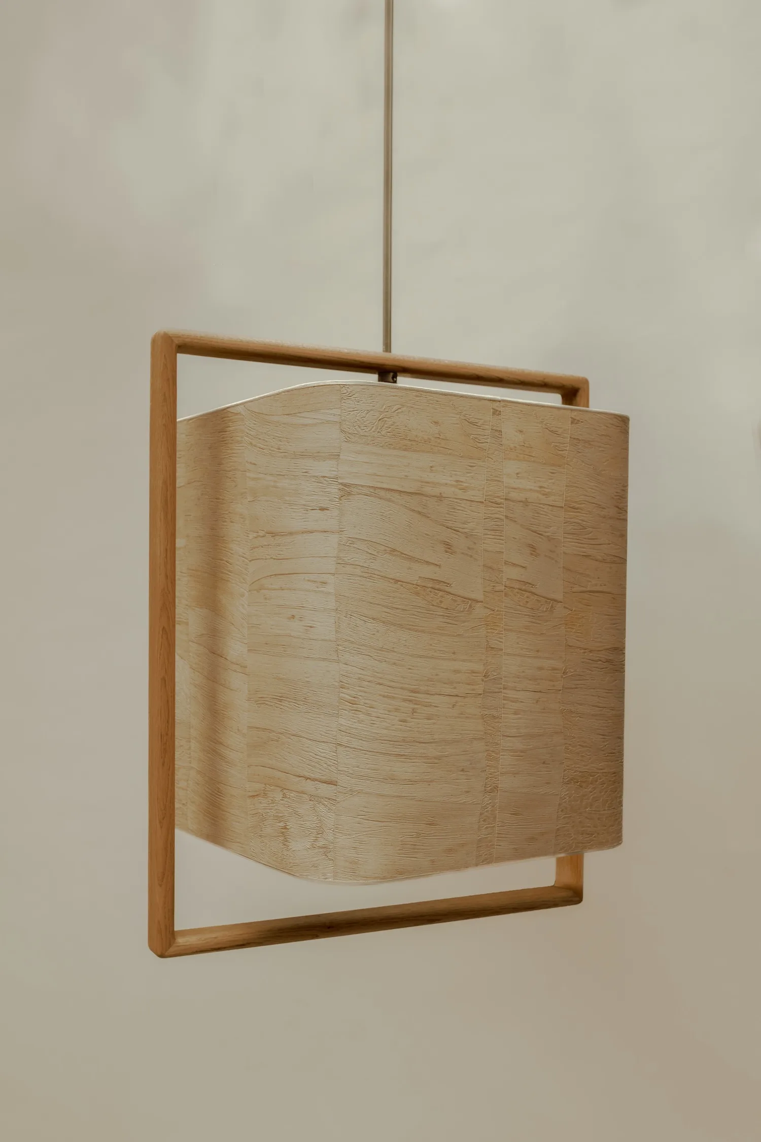 Close-up of the Lora ceiling light featuring a curved light wood veneer shade within a square wooden frame.