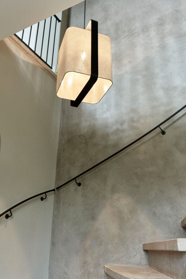 Lora ceiling light with a cube-shaped beige fabric shade and black metal frame, hanging over a stairwell.