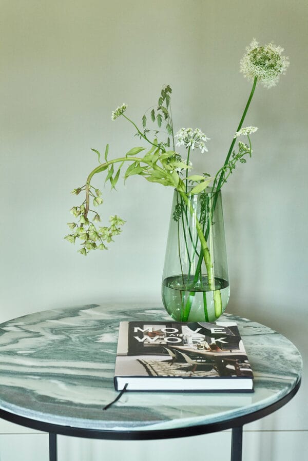 Detail of the Lucena side table showing green-veined marble surface, glass vase, and a book
