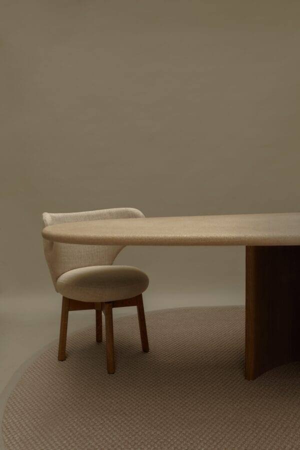 Beige Margaux dining chair paired with a round travertine table on a textured rug.