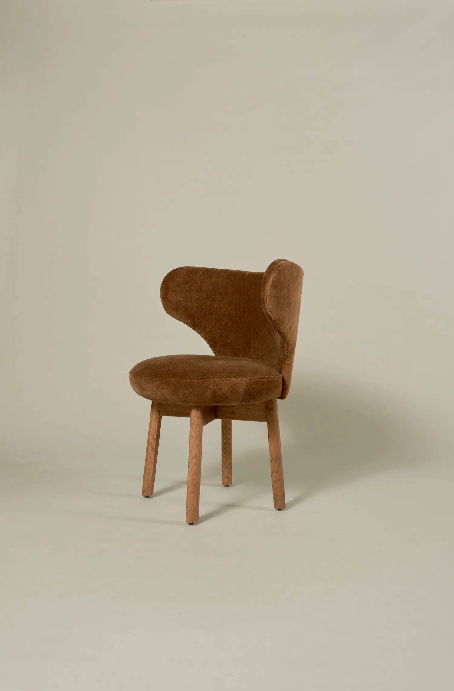 Angled view of the Margaux dining chair in brown velvet with a curved back.