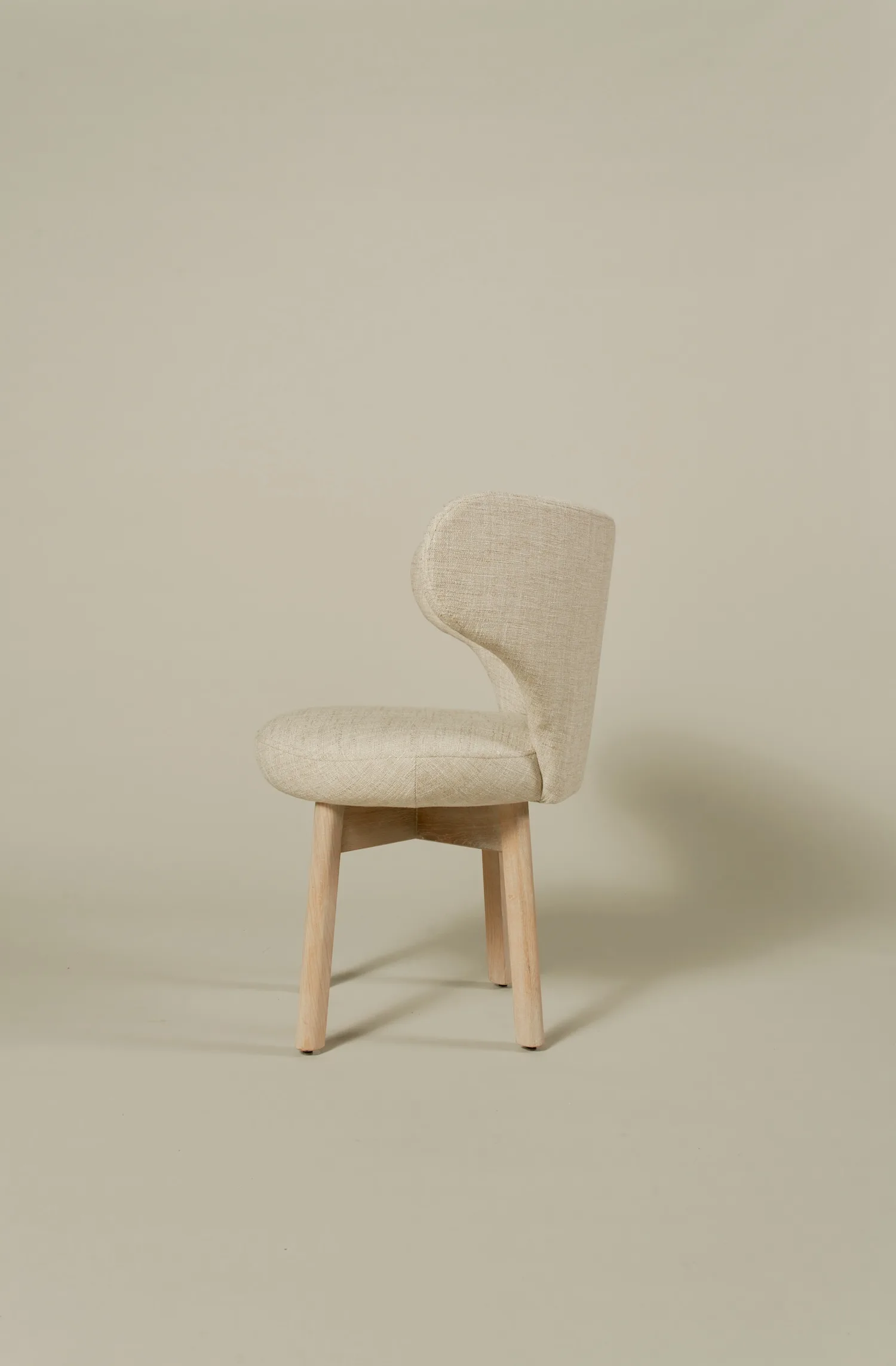 Side profile of a Margaux dining chair in neutral fabric and pale oak legs.