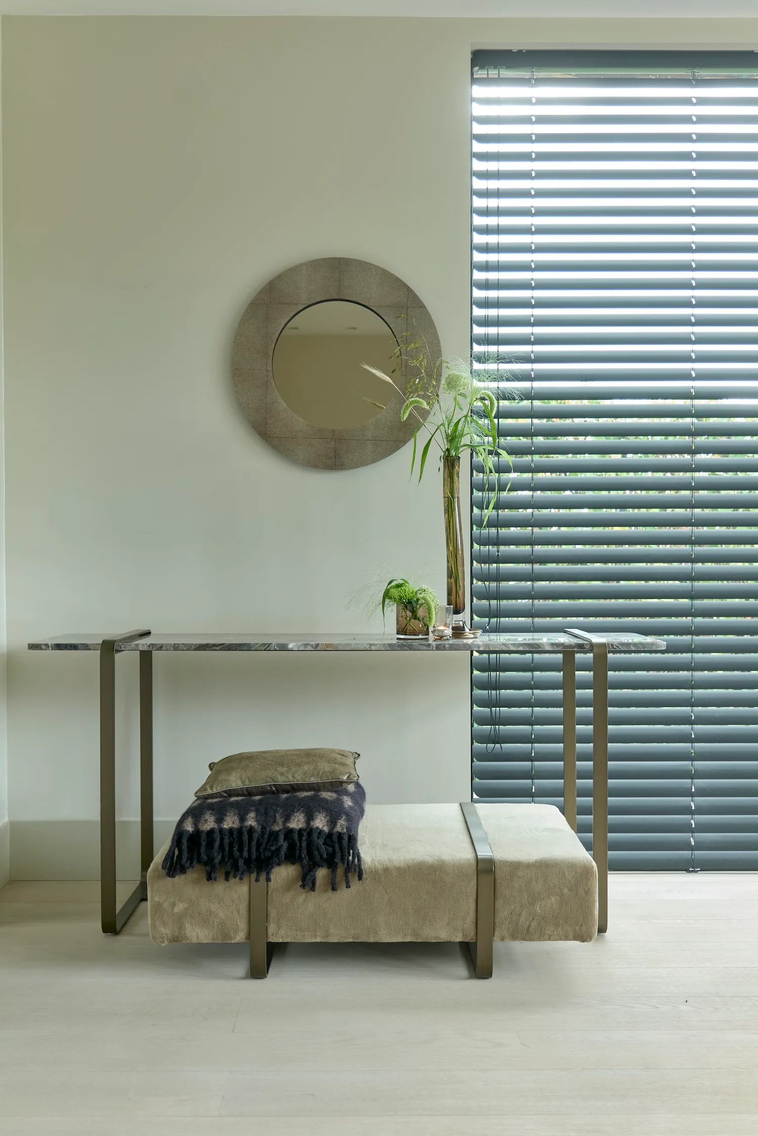 Monaco console with a marble top and bronze metal legs, styled with a mirror, vases, and a cushioned bench.