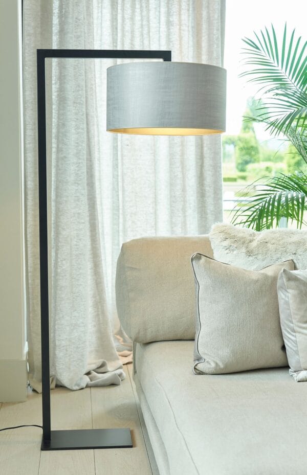 Murillo floor lamp with a light grey drum shade and black metal frame placed beside a beige sofa with cushions.