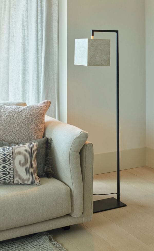 Murillo floor lamp with a cube-shaped stone-textured shade on a slim black frame next to a cream sofa.