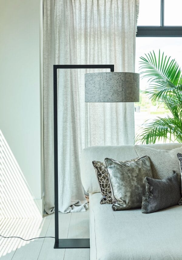 Murillo floor lamp with a dark speckled drum shade beside a modern sofa with metallic and patterned cushions.