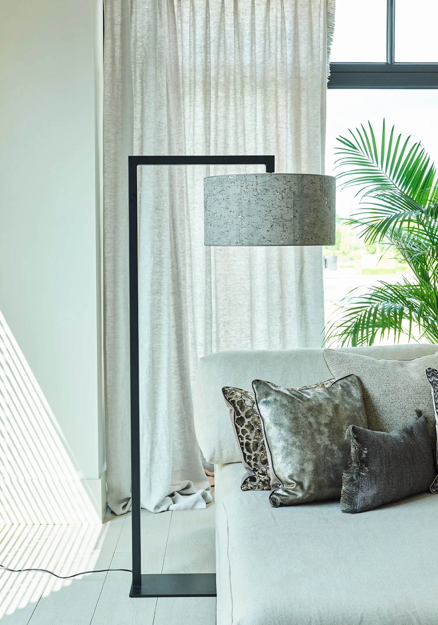 Murillo floor lamp with a dark speckled drum shade beside a modern sofa with metallic and patterned cushions.