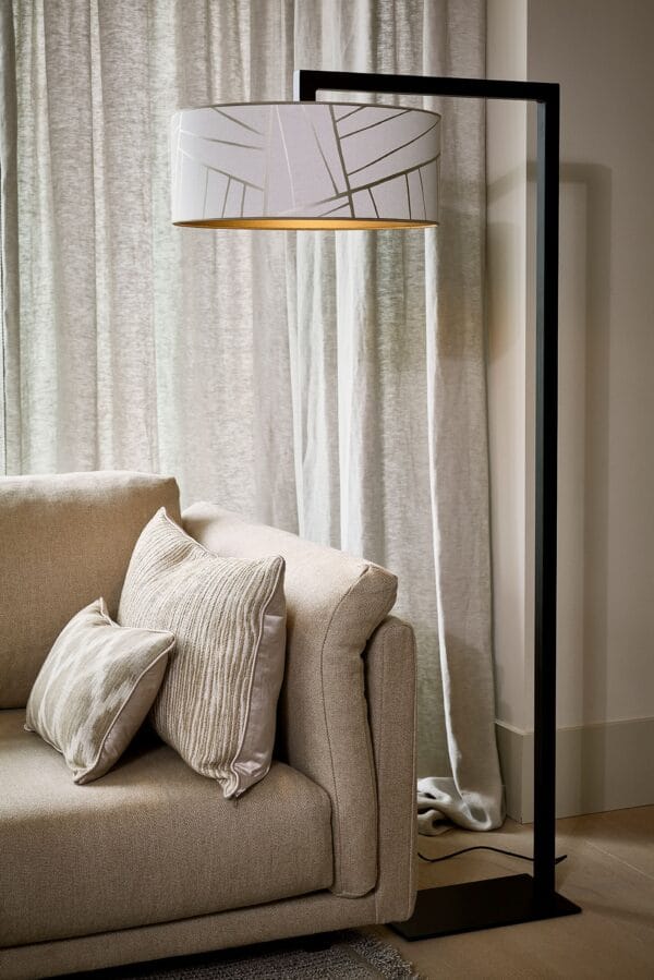 Murillo floor lamp with a white patterned drum shade and black frame positioned behind a soft beige sofa.
