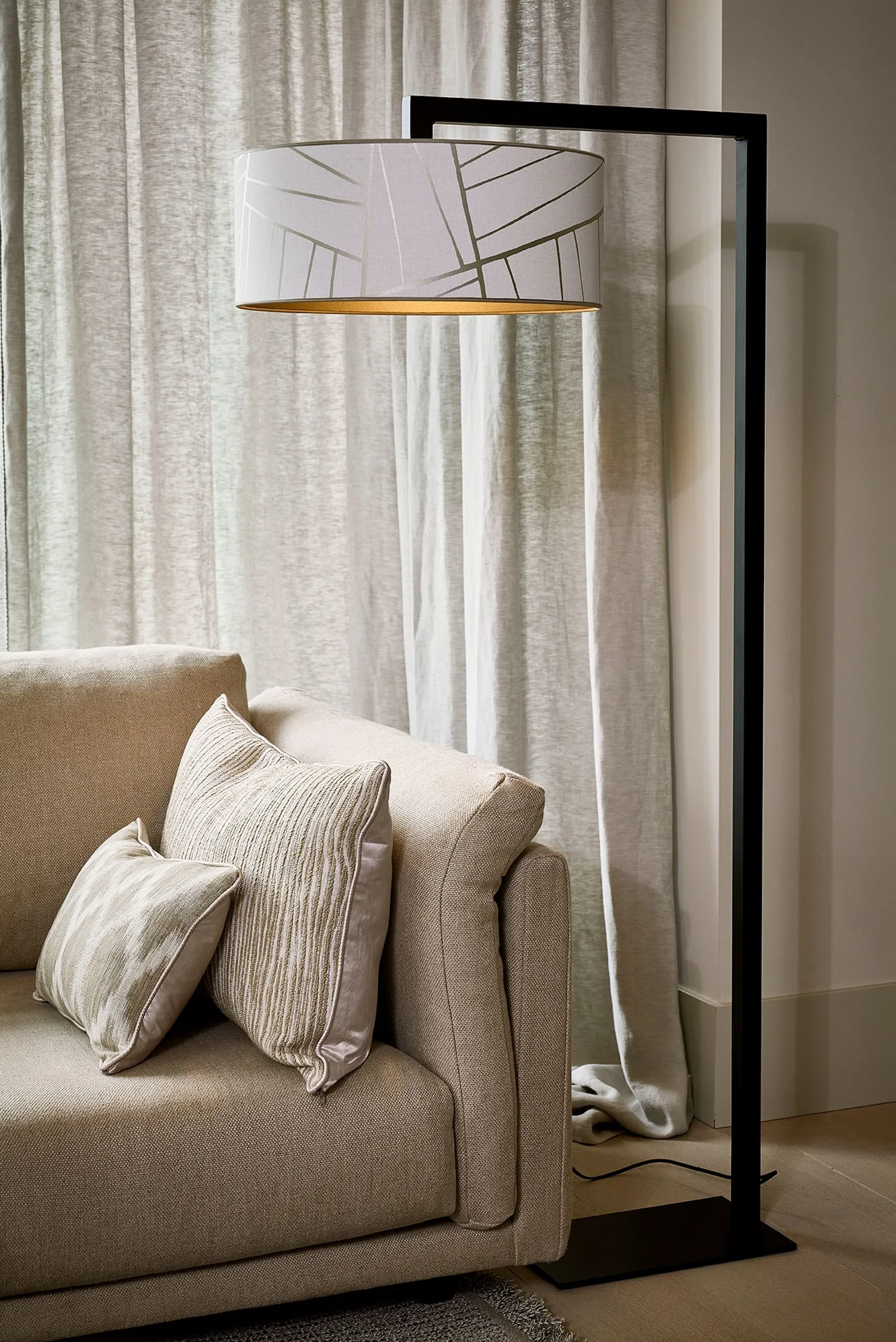 Murillo floor lamp with a white patterned drum shade and black frame positioned behind a soft beige sofa.