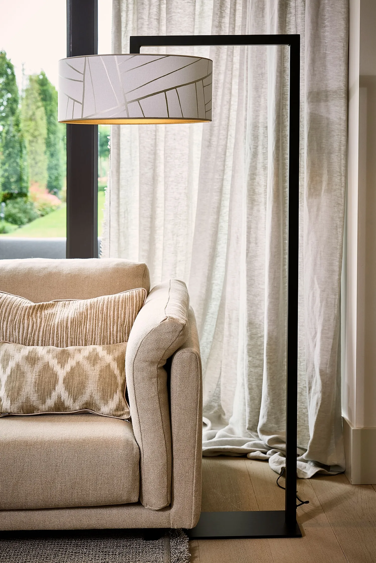 Murillo floor lamp with a geometric-patterned white shade beside a sofa, with a view of the garden outside.