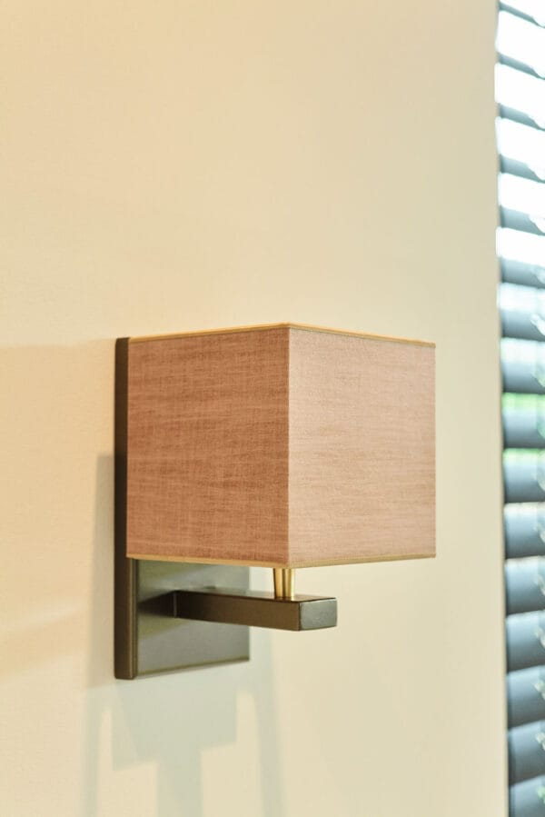 Murillo wall lamp with a pink linen square shade and brass accents on a black mount.