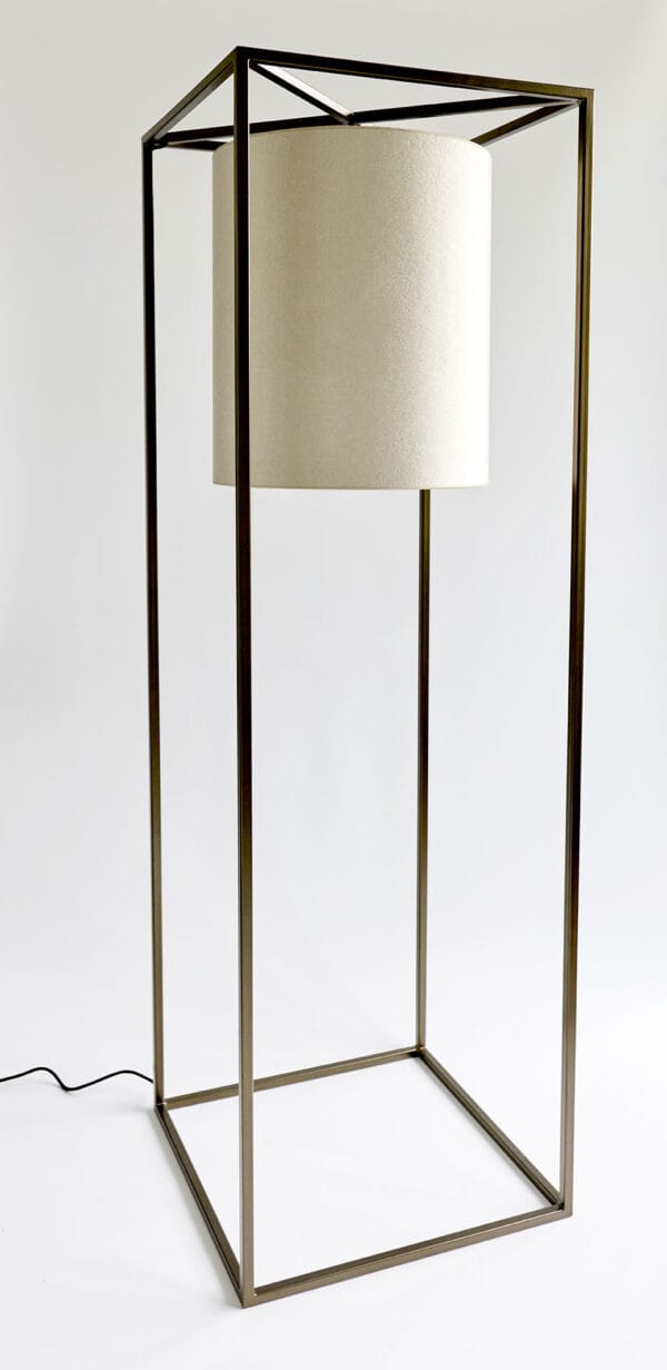 Studio view of the Noa floor lamp with a cylindrical cream shade inside a cube-shaped bronze frame.