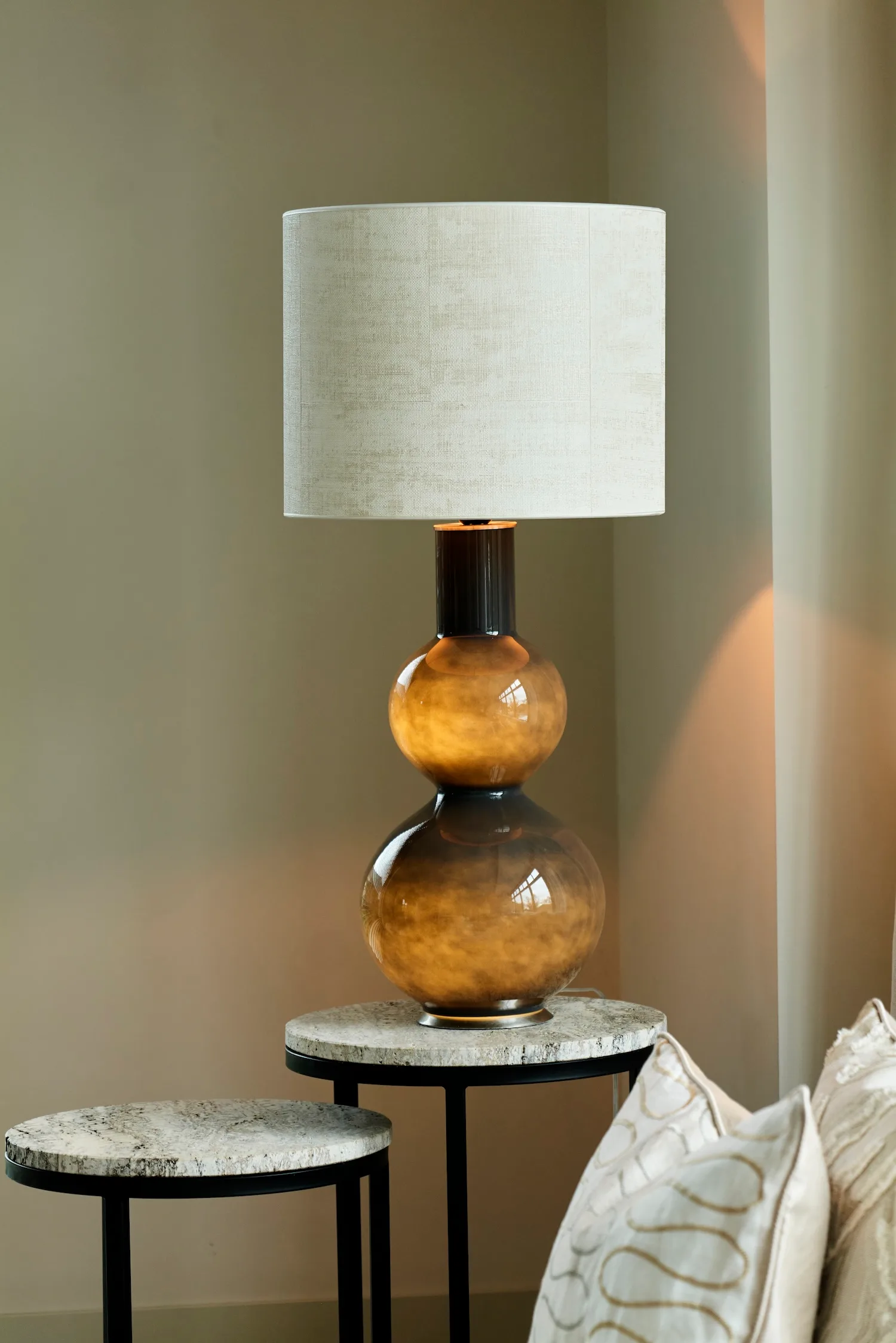 Olivia table lamp with a round off-white shade placed on a stone side table in a neutral-toned living room.