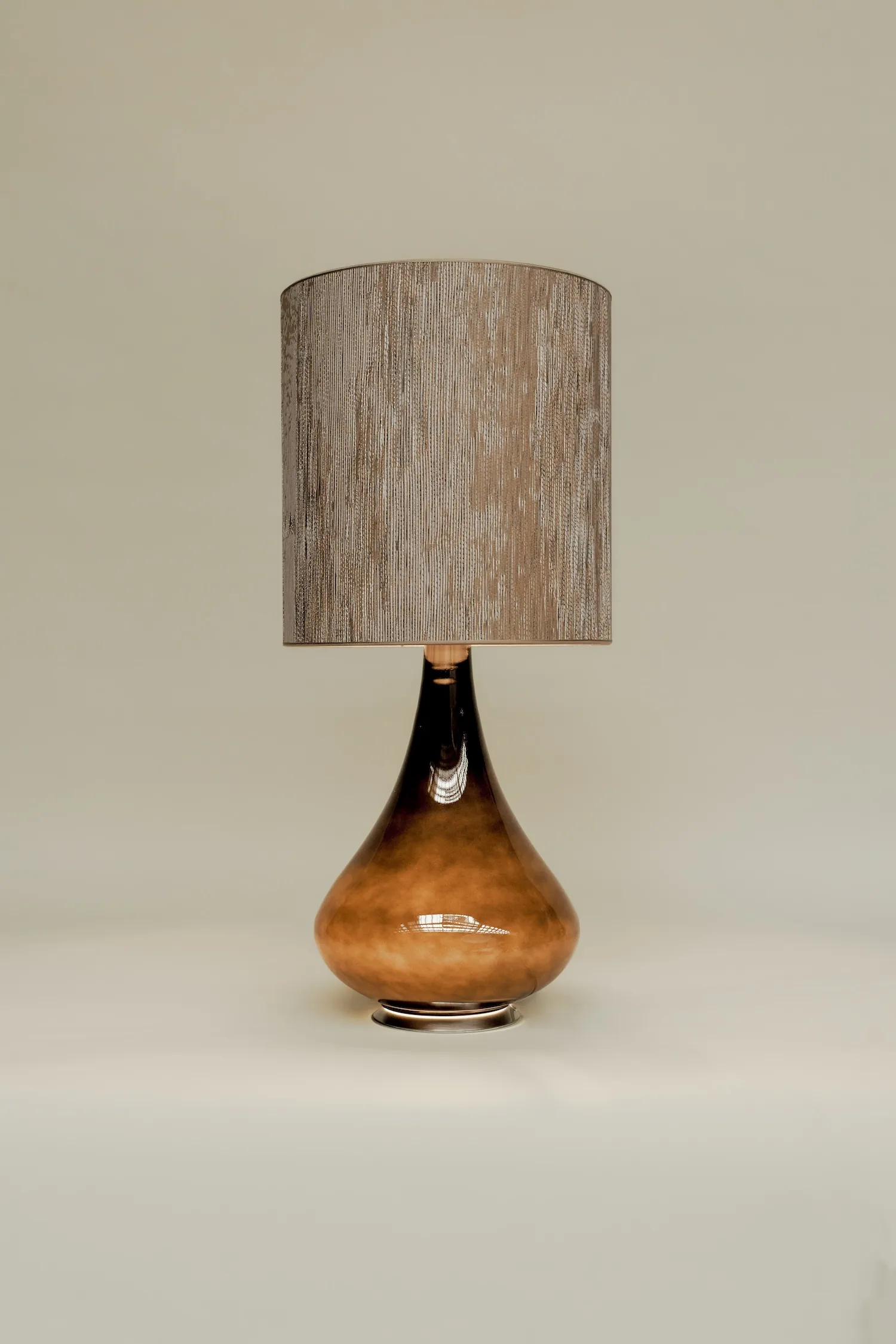 Studio shot of Paula lamp with a high-gloss brown glass base and vertically textured beige shade.