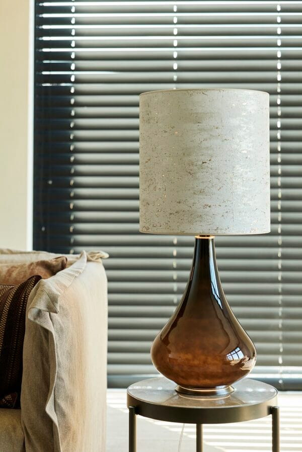 Paula table lamp beside a beige sofa, with a metallic brown base and a mottled light shade.