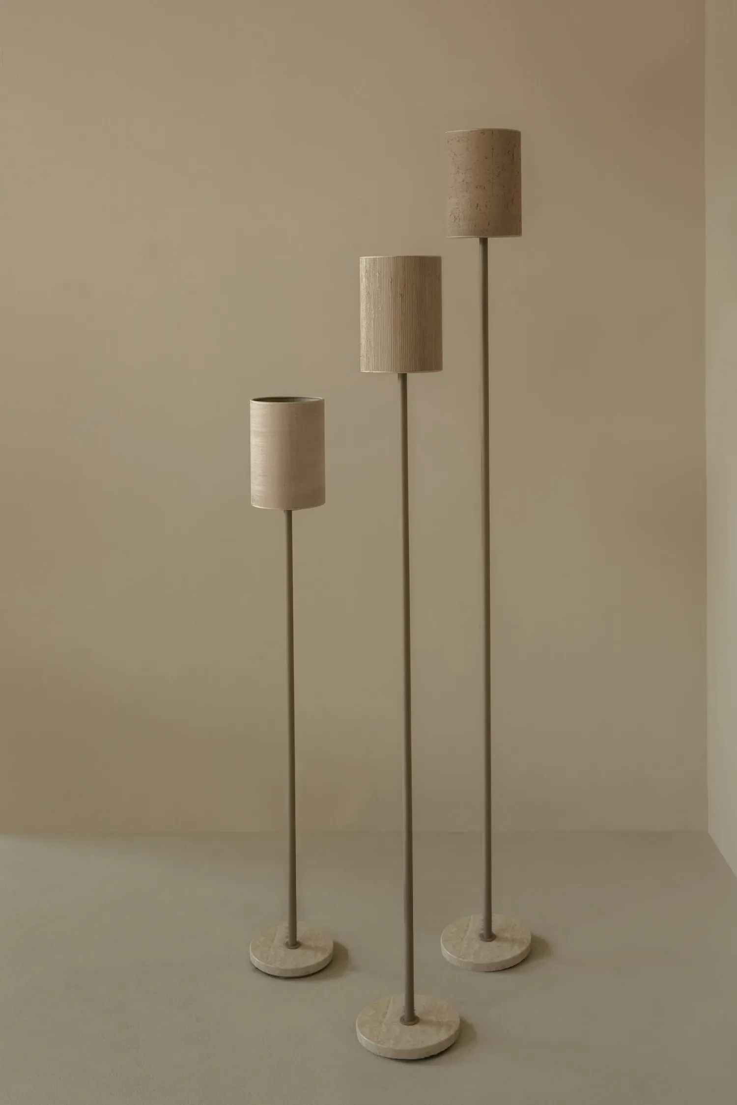 Three tall floor lamps with cylindrical fabric shades and round stone bases in neutral tones.