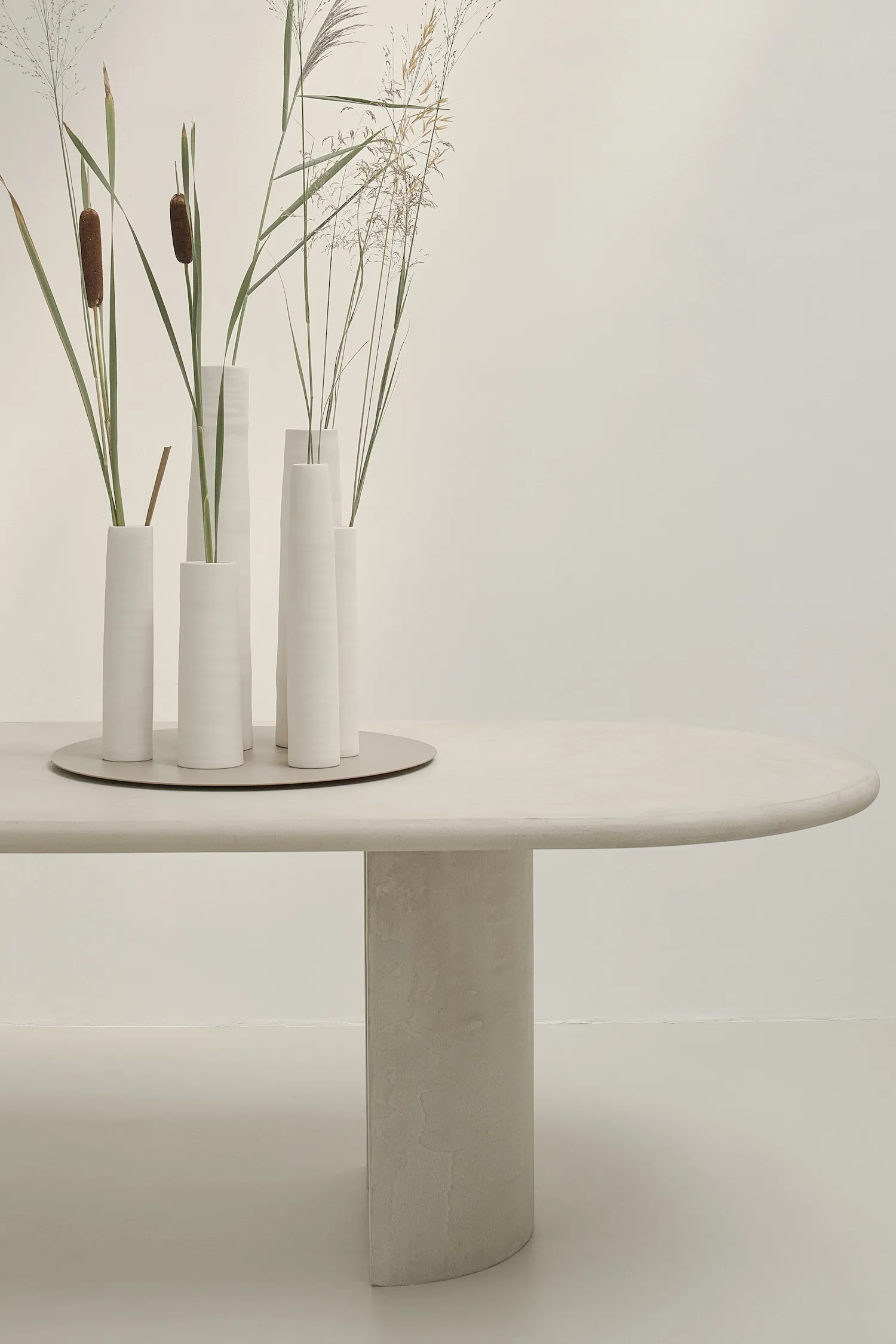Detail of one end of the Seine dining table featuring white ceramic vases and a rounded leg.