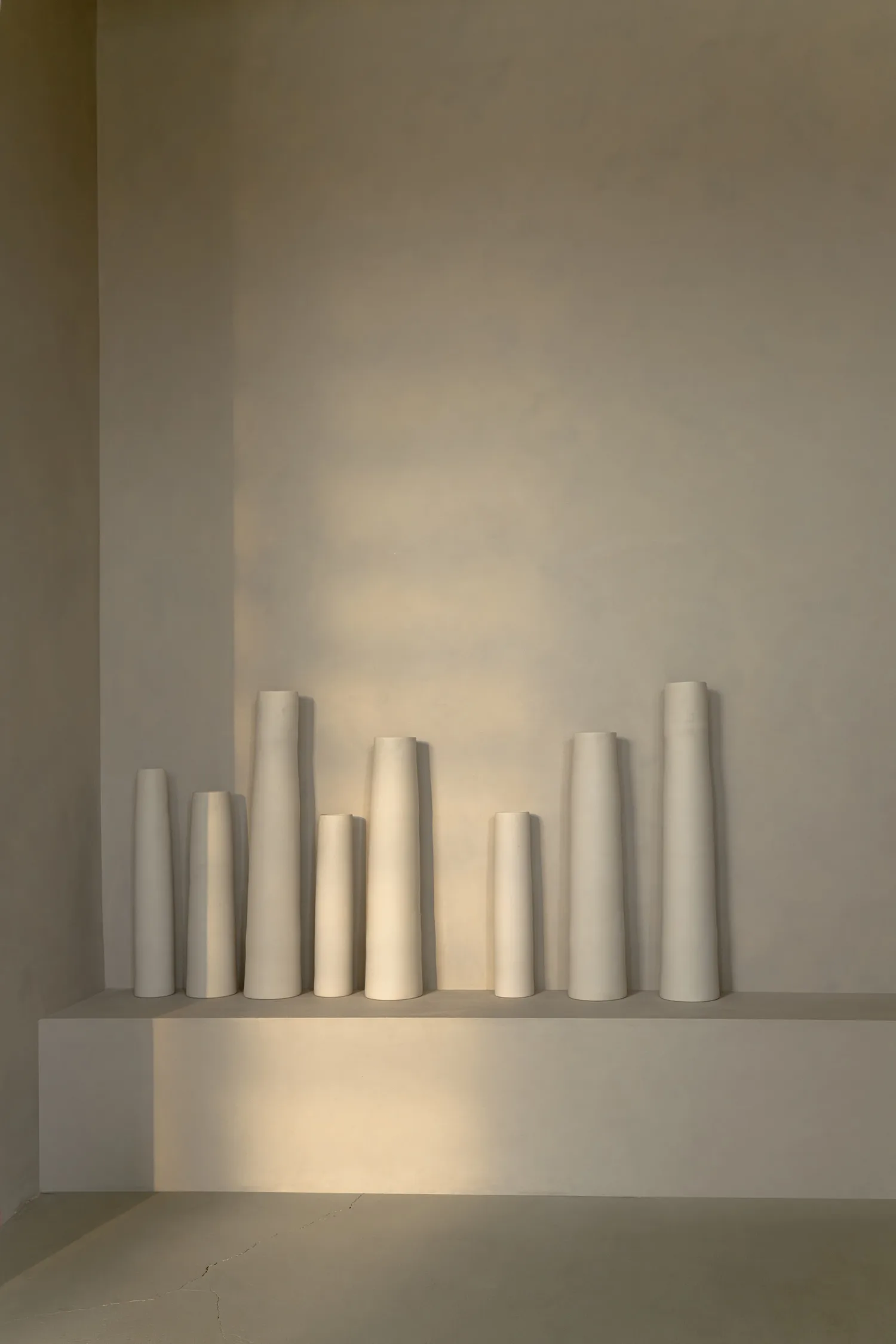 Collection of tall white vases arranged on a minimalist wall shelf in natural light.